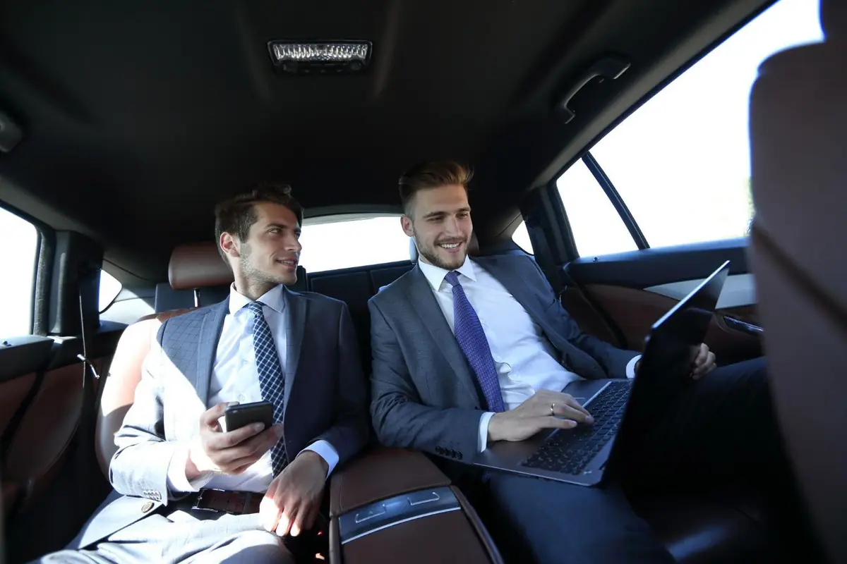 Two businessmen with a laptop and phone riding in the back seat of a car