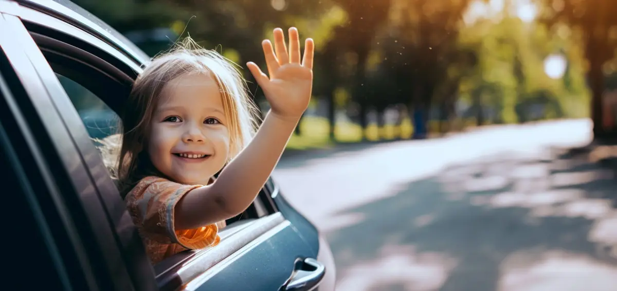 Smiling young girl waving from the rear window of a car